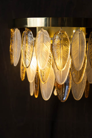 A detailed image of The Stunning Art Deco Glass Feather Wall Light displayed switched on against a dark wood wall
