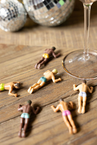 The Set of 6 Hunky Buddies Wine Glass Charms styled on a table next to a cocktail glass.
