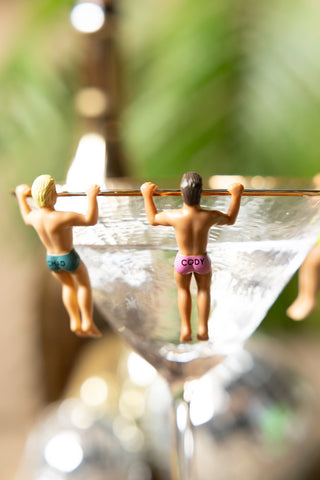 Two of the Set of 6 Hunky Buddies Wine Glass Charms styled on a cocktail glass.