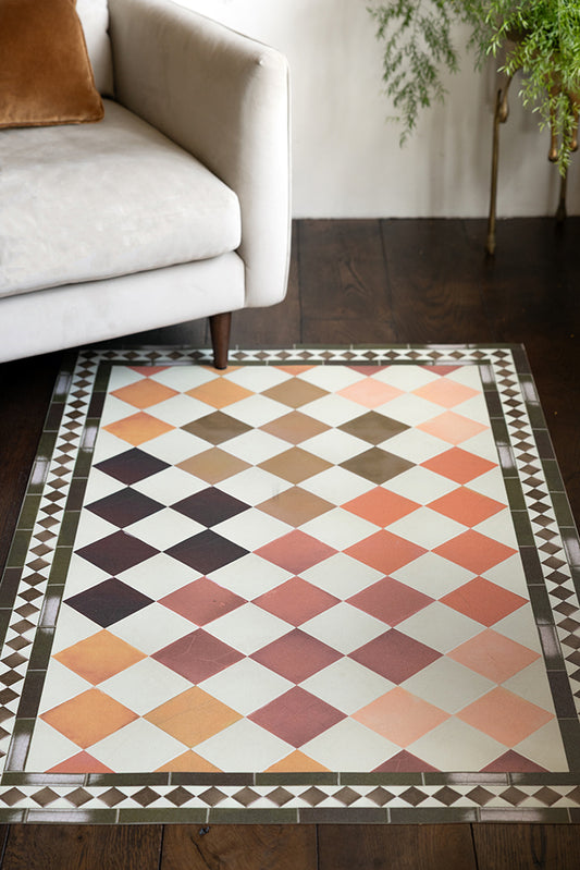 The Terracotta Checkered Durable Floor Mat shown on a dark wood floor against a beige velvet armchair. 