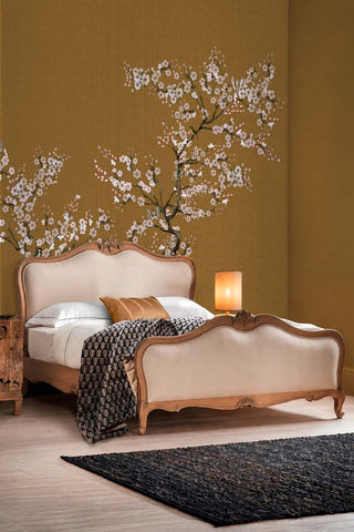 The Blossom Mischief Mural Wallpaper in Antique Gold shown in a bedroom with a French-style bed.