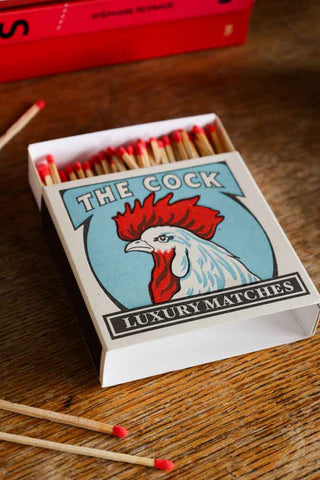 Lifestyle image of The Cock Luxury Matches displayed on a wooden table. 