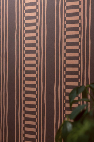 Close up detail of the The Curiosity Shop Stripe Wallpaper in Aubergine, with a plant in the corner. 