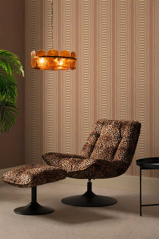 The Curiosity Shop Stripe Wallpaper in Blush shown in a living room with a leopard velvet swivel chair, matching footstool and an amber glass ceiling light. 