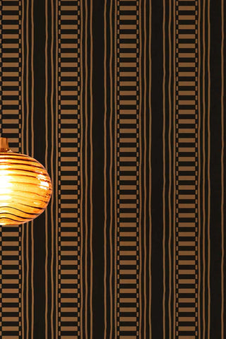 Close up of the The Curiosity Shop Stripe Wallpaper in Noir with an amber glass pendant light shown at the side of the image. 