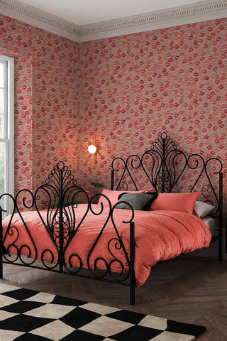 The Kiss Me Lipstick Wallpaper shown in a bedroom with a black ornate metal bed frame. 