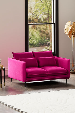 The Lola 2 Seater Sofa in Harry's Pink Velvet styled with a rug, floor lamp and side table in front of a window.