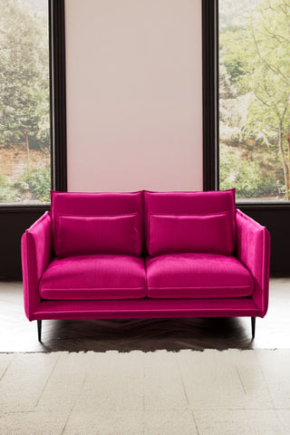 The Lola 2 Seater Sofa in Harry's Pink Velvet styled with a rug in front of two windows.