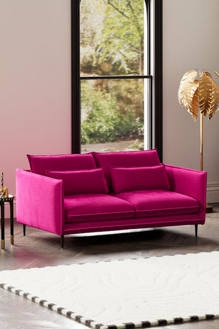The Lola 3 Seater Sofa in Harry's Pink Velvet styled with a rug, side table and floor lamp in front of a window.