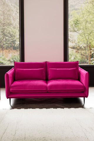 The Lola 3 Seater Sofa in Harry's Pink Velvet styled with a rug in front of two windows.