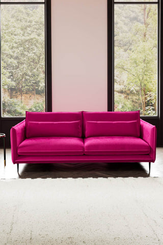 The Lola 4 Seater Sofa in Harry's Pink Velvet styled with a rug in front of two windows.