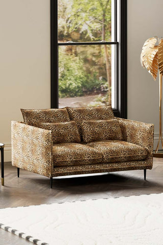 The Lola 2 Seater Sofa in Leopard Print Velvet styled with a rug, floor lamp and side table in front of a window.