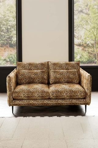 The Lola 2 Seater Sofa in Leopard Print Velvet styled with a rug in front of two windows.