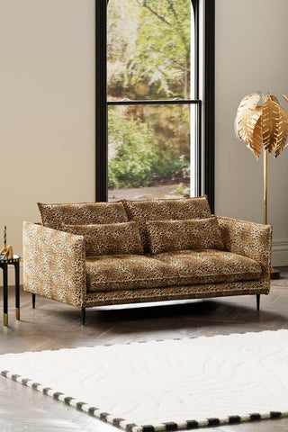 The Lola 3 Seater Sofa in Leopard Print Velvet styled with a rug, side table and floor lamp in front of a window.