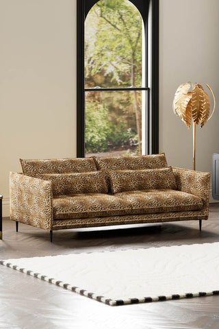 The Lola 4 Seater Sofa in Leopard Print Velvet styled with a rug and floor lamp in front of a window.