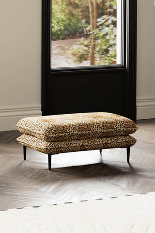 The Lola Footstool in Leopard Print Velvet with a rug in front of a window.
