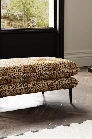 Close-up of The Lola Footstool in Leopard Print Velvet styled with a rug, with a window in the background.