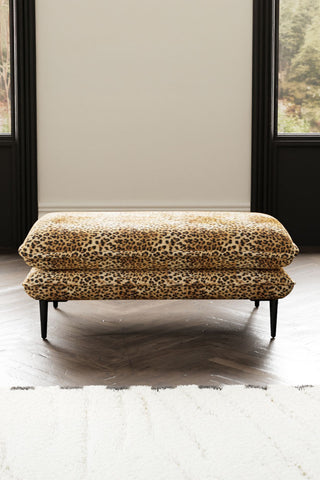 The Lola Footstool in Leopard Print Velvet with a rug, with two windows in the background.