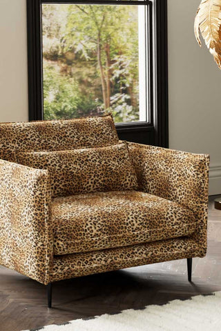 Close-up of The Lola Snuggle Seat in Leopard Print Velvet styled with a rug and floor lamp by a window.