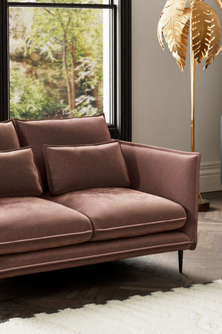 Close-up of one side of The Lola 2 Seater Sofa in Luxe Pink Velvet, styled with a rug and floor lamp, with a window in the background.