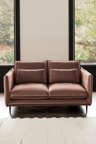 The Lola 2 Seater Sofa in Luxe Pink Velvet styled with a rug in front of two windows.
