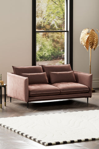 The Lola 3 Seater Sofa in Luxe Pink Velvet styled with a rug, floor lamp and side table in front of a window.