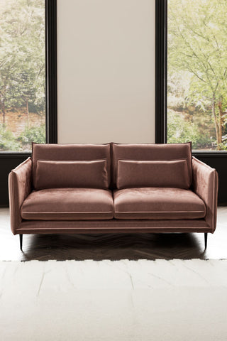 The Lola 3 Seater Sofa in Luxe Pink Velvet styled in front of two windows.