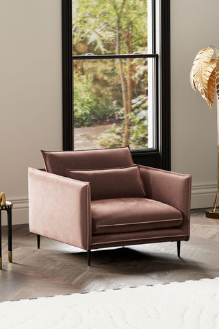 The Lola Snuggle Seat in Luxe Pink Velvet styled with a rug, side table and floor lamp in front of a large window.