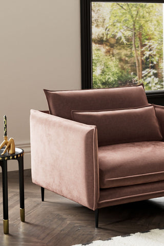 The Lola Snuggle Seat in Luxe Pink Velvet styled with a side table and candle holder with a window in the background.