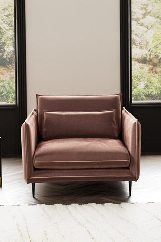 The Lola Snuggle Seat in Luxe Pink Velvet styled with a rug with two windows in the background.