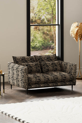 The Lola 2 Seater Sofa in Tiger Print Velvet styled with a rug, side table and floor lamp in front of a window.