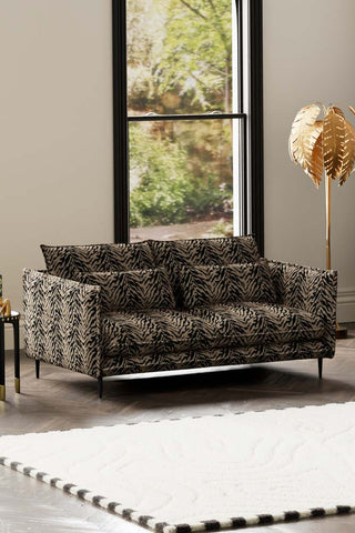 The Lola 3 Seater Sofa in Tiger Print Velvet styled with a rug, side table and floor lamp in front of a window.