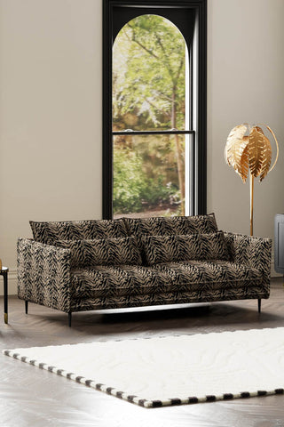 The Lola 4 Seater Sofa in Tiger Print Velvet styled with a rug, floor lamp and side table in front of a window.