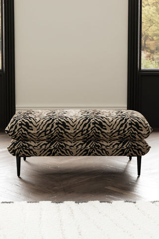 The Lola Footstool in Tiger Print Velvet styled behind a rug, with two windows in the background.