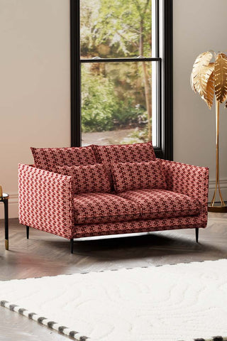 The Lola 2 Seater Sofa in Woven Red & Pink Lips Velvet styled with a rug, side table and floor lamp, in front of a window.