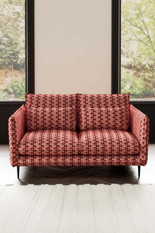 The Lola 2 Seater Sofa in Woven Red & Pink Lips Velvet styled with a rug in front of two windows.