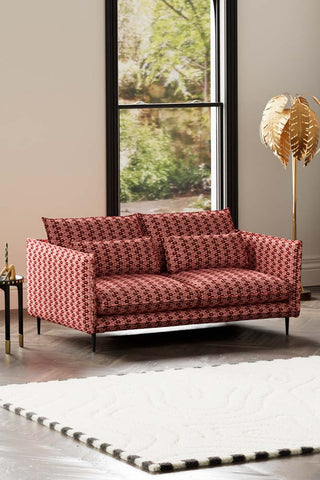 The Lola 3 Seater Sofa in Woven Red & Pink Lips Velvet styled with a rug, floor lamp and side table in front of a window.