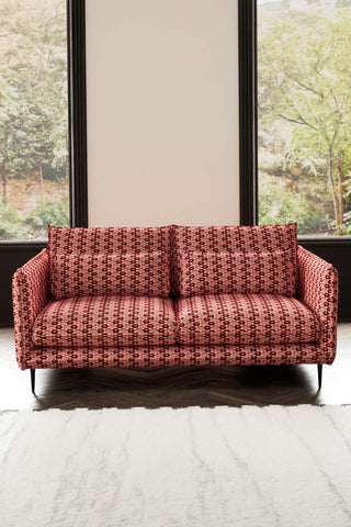 The Lola 3 Seater Sofa in Woven Red & Pink Lips Velvet styled in front of two windows.