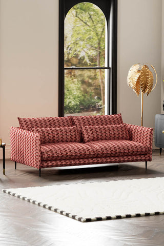The Lola 4 Seater Sofa in Woven Red & Pink Lips Velvet styled with a rug and floor lamp with a window in the background.