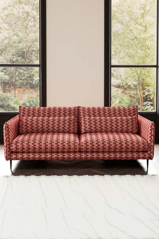 The Lola 4 Seater Sofa in Woven Red & Pink Lips Velvet behind a rug, with two windows in the background.