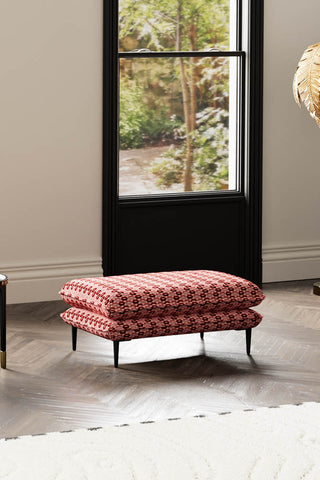 The Lola Footstool in Woven Red & Pink Lips Velvet styled on a wooden floor with a window in the background.