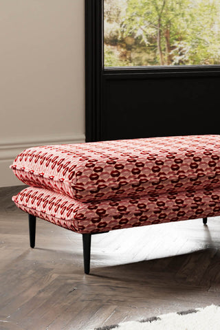 Close-up of The Lola Footstool in Woven Red & Pink Lips Velvet styled on a wooden floor.