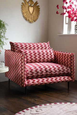 The Lola Snuggle Seat in Woven Red & Pink Lips Velvet styled in the corner of a room with various accessories in the  background.