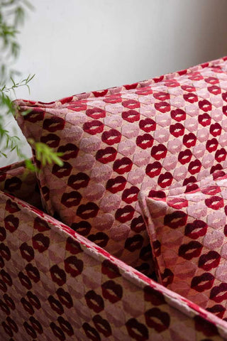 Close-up of the cushions of The Lola Snuggle Seat in Woven Red & Pink Lips Velvet styled next to a plant.