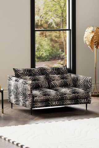 The Lola 2 Seater Sofa in Zebra Print Velvet styled with a  rug, floor lamp and side table in front of a window.