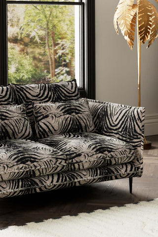 Close-up of one side of The Lola 2 Seater Sofa in Zebra Print Velvet, styled with a rug and floor lamp.