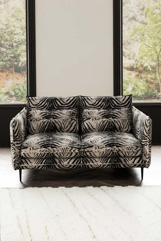 The Lola 2 Seater Sofa in Zebra Print Velvet styled with a rug in front of two windows.