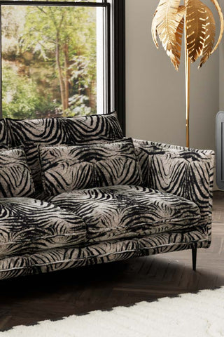 Close-up of one side of The Lola 3 Seater Sofa in Zebra Print Velvet, styled with a rug and floor lamp in front of a window.