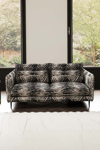 The Lola 3 Seater Sofa in Zebra Print Velvet styled with a rug in front of two windows.