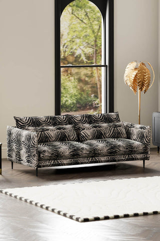 The Lola 4 Seater Sofa in Zebra Print Velvet styled with a rug and floor lamp in front of a window.
